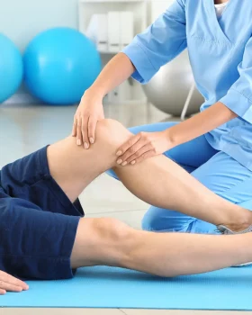 Médecin en train d'examiner le genoux d'un patient en tenue de sport et allongé sur un tapis de sol